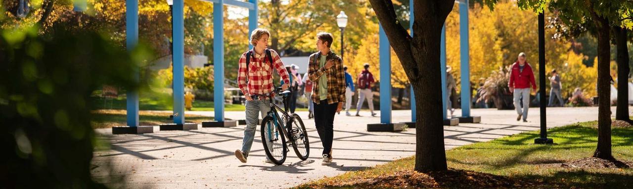 student walking next to student with bicycle under the Transformational Link